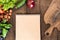 Overhead view of raw vegetables, chopping board and blank notepad on wooden table