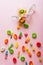 Overhead view of scattered fallen multi colored sugar candies with open jar on pink background