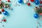 Overhead view of vibrant baubles, frosty pine, holly berries, and snowflake decor on a pastel blue surface