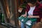 Overhead view of a woman gardener holding suitcase with gardening tools, sitting at the entrance to a wooden greenhouse with grown