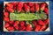 Overhead view of a wooden tray with a bunch of green wild asparagus surrounded by fresh strawberries.