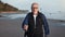 Overjoyed 70s grandfather backpacker Nordic walking stick healthcare hiking trekking sunny sea beach