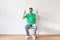 Overjoyed arab man sitting on chair and pointing two fingers up, offering space for your advertisement, light wall