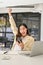 Overjoyed Asian businesswoman at her desk, looking at her phone screen, raising hand