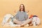 Overjoyed Caucasian woman posing near heap of multicolored unsorted clothes isolated over beige background clenched fists