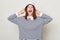 Overjoyed cheerful brown haired adult woman wearing striped shirt and panama standing isolated over gray background looking at