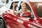 Overjoyed driver woman smiling and showing new key while sitting in car showroom