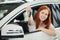 Overjoyed driver woman smiling and showing new key while sitting in car showroom