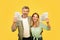 Overjoyed european middle aged couple holding fans of dollar cash, smiling at camera on yellow studio background