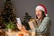 Overjoyed funny woman wearing knitted shirt and Santa hat holding gift box sitting at home with x-mas Christmas decoration