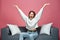 Overjoyed lucky young girl celebrating win with raised arms, screaming with euphoria, sitting on sofa