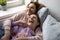 Overjoyed mother and laughing teenage daughter relaxing on bed together