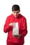 Overjoyed teenager opening white paper bag looking into package. Caucasian teen dressed in red hoodie isolated on white
