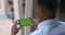 Overshoulder view of afro american guy holding phone in horizontal landscape mode. Guy looking and touching green