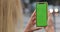 Overshoulder view of unknown woman holding smartphone green screen with both hands. Close up view of female person using