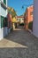 Overview of colorful terraced houses, lamp and bushes in an alley in Burano.