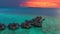 Overwater villas at the time amazing sunset in tropical sea with coral reef. Aerial drone view.