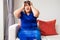 An overweight Asian woman is sitting on the sofa in the living room. And holding hands in the head due to headaches from migraines