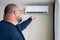 Overweight exhausted man using remote control to switch on air conditioner at home.