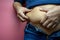 Overweight fat woman touching obese belly isolated on a pink background in Studio, closeup. Weight losing, obesity, cellulite,