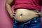 Overweight fat woman touching obese belly isolated on a pink background in Studio, closeup. Weight losing, obesity, cellulite,