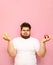 Overweight funny guy stands with apples in his hands on a pink background and makes a funny face wearing a white T-shirt. Vertical