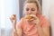 An overweight girl is eating a sandwich and holding a centimeter-long ribbon. Junk food.