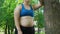 Overweight girl leaning on tree, tired after jogging, daily workouts outdoors