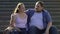 Overweight male hugging his beautiful girlfriend, resting on stairs outdoor date