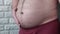 An overweight man demonstrates a big belly with obesity, a man slaps his hand on a fat belly. Fat man