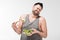 Overweight man holding bowl of salad and making face expression isolated on white