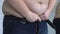 Overweight man zipping up jeans, suffering from stomach fat, hormonal disease