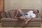 An overweight, unshaven and lazy man of mixed race sleeps on the couch, still holding his cellphone