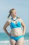 Overweight woman in blue bikini standing arms akimbo outdoors