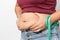 Overweight woman check out his body fat with green measuring tape for obesity on gray background,