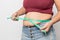 Overweight woman check out his body fat with green measuring tape for obesity on gray background,