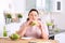 Overweight woman eating sandwich instead of salad at table in kitchen