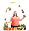 Overweight woman juggling vegetables behind a table with fruit a