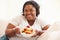 Overweight Woman Sitting On Sofa Eating Bowl Of Fresh Fruit