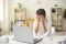 Overworked female manager closes face with tired hands sitting in front of laptop in bright office.