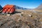 Owl River emergency shelter in remote arctic wilderness with a backpack in front of it . Sunny day in Akshayuk Pass