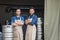 Own small business. Two guys crossed arms over chest and stand near metal barrels in brewery warehouse