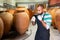 Owner in protective mask of winery standing with wine in wooden barrels cellar