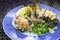 Oyster Rockefeller, baked with herb butter, cheese and spinach, served with salad and lemon slices on a blue plate, selected focus