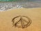 Pacifist sign on the wet sand at the water`s edge