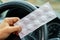 Pack of pills in the hands of the driver on a blurred background of the steering wheel in the car