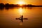 Paddle boarding lady silhouette having oar in hands on lake with charming sunset in background covering water with