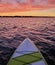 A Paddleboard floating on calm water at dusk with the colorful light of sunset shining on the wind whipped ripples