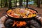 paella pan with colorful ingredients over open campfire