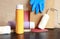 Paint bottles, paint roller, blue gloves and sandpaper. Items needed for repairs on a wooden table